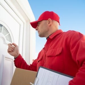 A delivery man in red uniform knocking on a white door carrying a package.